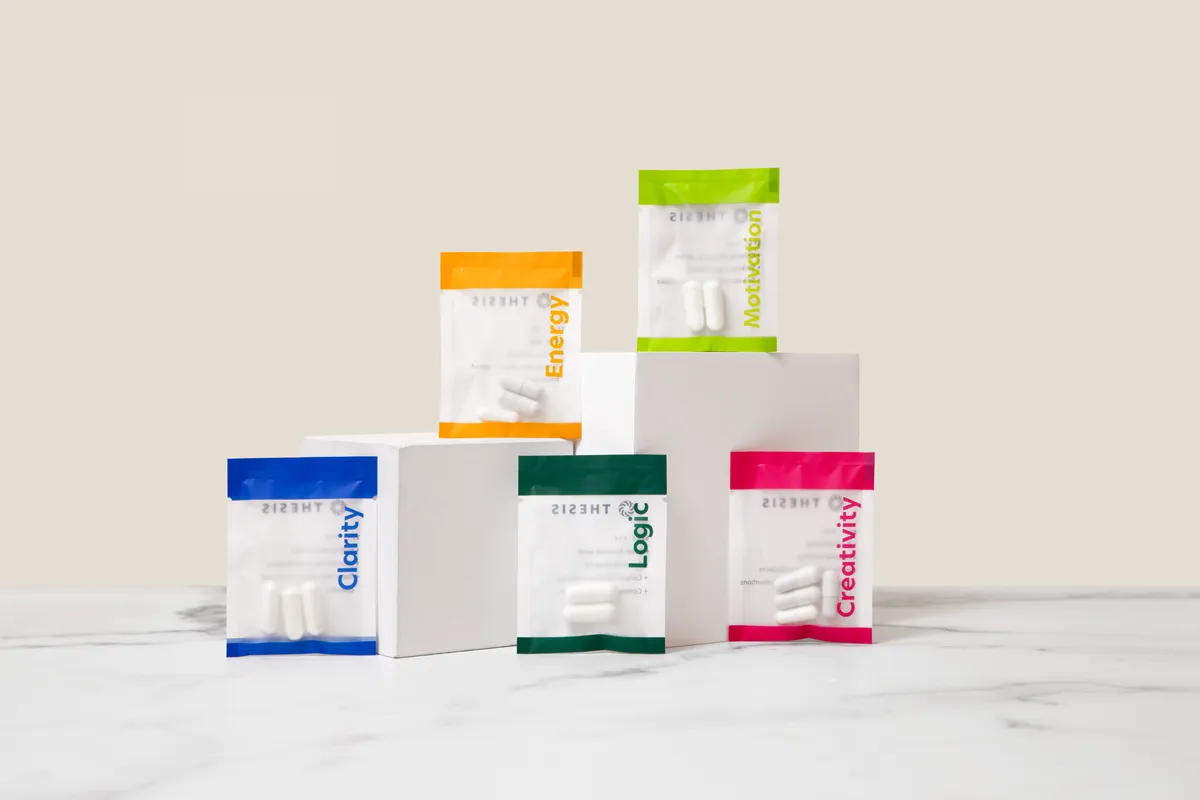 Five colour-coded printed capsule sachets standing on white blocks on a marble surface