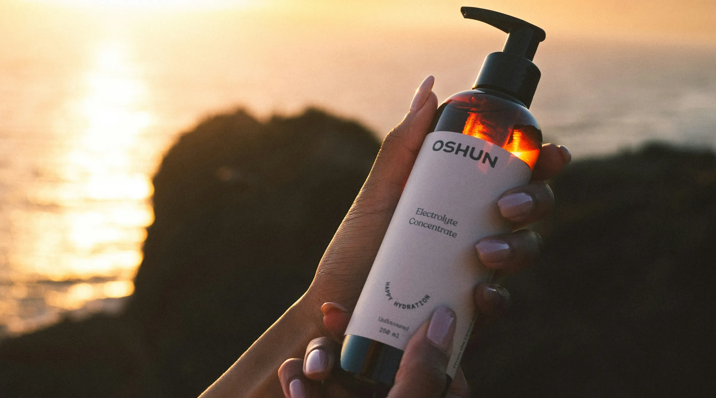 Amber pump bottle with a cream label held up at sunset