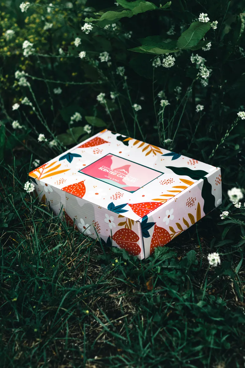 Floral printed corrugated mailer box with a pink label resting in long grass